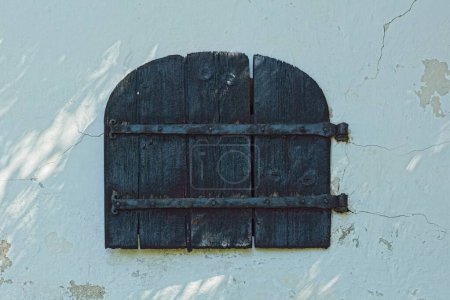 An old wooden door with arch on a white stone wall.