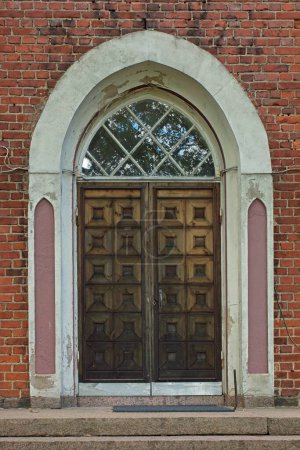 An old wooden door with white arch frame on a red brick wall.