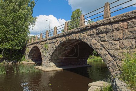 Self-supporting old stone bridge with arches over river in summer.