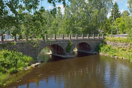 Self-supporting old stone bridge with arches over river in summer.