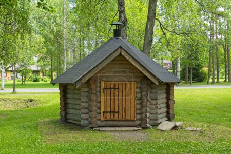 Small log cabin with grill inside and chimney on roof.