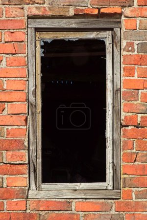 Closeup of damaged glassless window on the wall of an abandoned red brick building.
