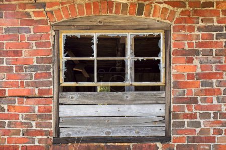 Nahaufnahme eines beschädigten glaslosen Fensters an der Wand eines verlassenen roten Backsteingebäudes.