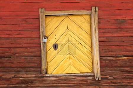 Old wooden yellow door on a red painted log building.
