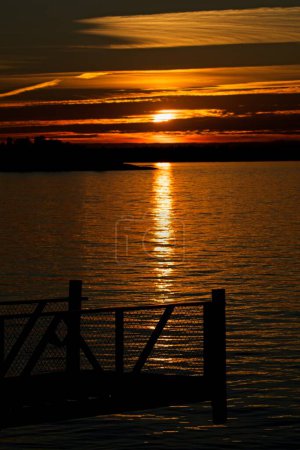 Sunset with clouds in the sky in autumn with pier silhouette at seashore on the island of Torra Lv, Espoo, Finland.