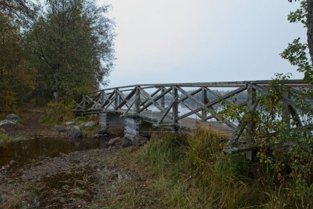 Puente peatonal de madera con cielo nublado en otoño, Kyynrnjuova, Parque Nacional Liesjrvi, Tammela, Finlandia.
