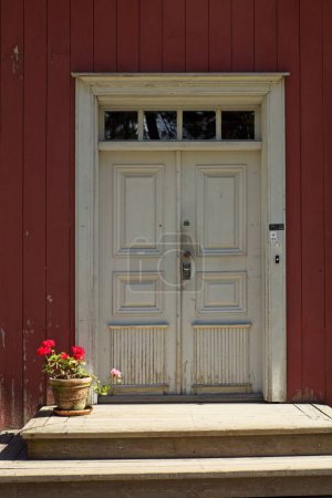 Old white double door with windows on top on a red painted wooden building.