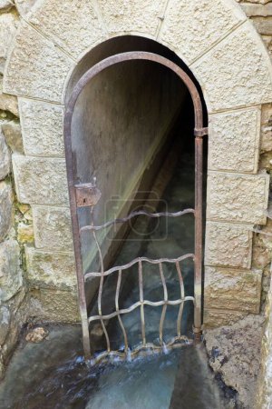 Old metal gate to narrow dark tunnel that goes to a lake, Seven Springs, Rhodes, Greece.