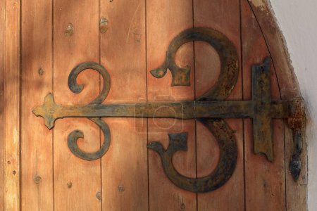 Decorative rustic metal hinge on old wooden door on a stone building.