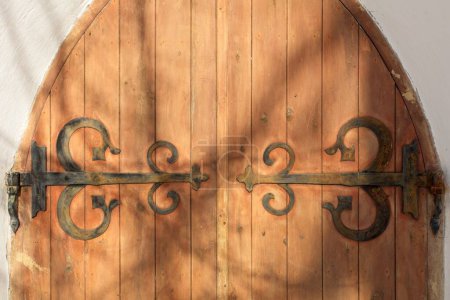 Decorative rustic metal hinges on old wooden doors on a stone building.