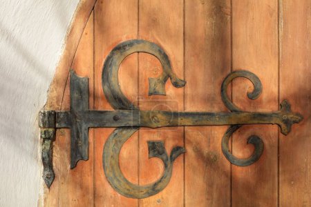 Charnière en métal rustique décorative sur une vieille porte en bois sur un bâtiment en pierre.