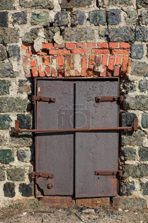Rusty metal doors barred shut on old red brick and stone building, Taalintehdas, Finland.