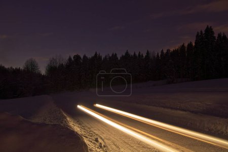 Long exposed night image of car with lights on a dark road through a forest.