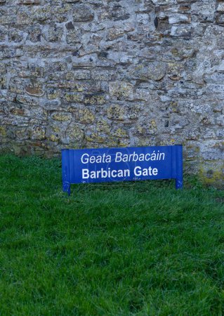 Photo for Blue Barbican Gate sign on the green lawn in fron of an old, grey, stone wall - Royalty Free Image