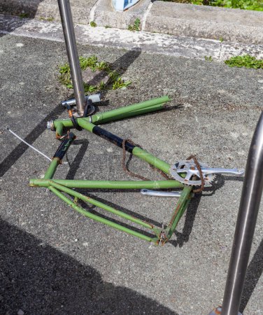 Green bibyble frame chained to a metal bar on the ground. The bike is damaged with the chain hanging on the frame