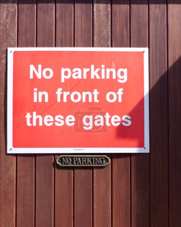 Two no parking signs on a wooden gate on a sunny day. There is a shadow of a roof on the sign
