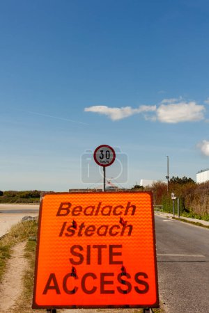 Orange Site Access Verkehrsschild mit einem Tempolimit-Schild dahinter neben einer Straße unter wolkenlosem blauen Himmel.
