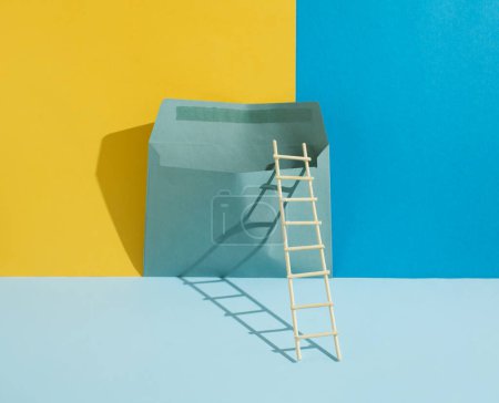 Foto de Composición surrealista minimalista hecha de una escalera de madera y un sobre sobre sobre fondo azul, azul pastel y amarillo. Concepto de comunicación y mensajería. Diseño creativo minimalista. Copiar espacio. - Imagen libre de derechos
