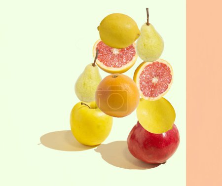 Un patrón hecho de frutas aisladas, una naranja, un pomelo, una manzana, una granada, peras y limones sobre un fondo verde y naranja. Espacio de copia, concepto de fruta mínima. Dieta sana y equilibrada.