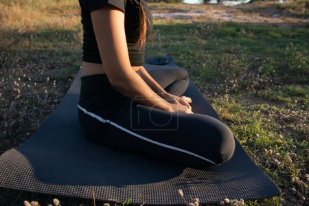 Beautiful young female practicing yoga in nature on a green grass during golden hour in summertime in the mountain village El Papiol, near Barcelona, Spain 