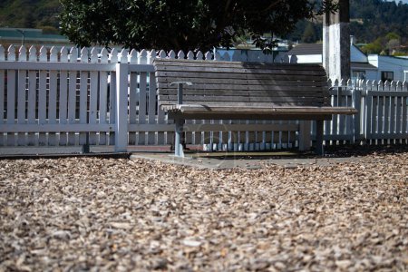 Téléchargez les photos : Un banc de parc unique dans une aire de jeux pour enfants, inoccupé par une journée ensoleillée abandonnée, peu fréquentée, vacante et oubliée. - en image libre de droit