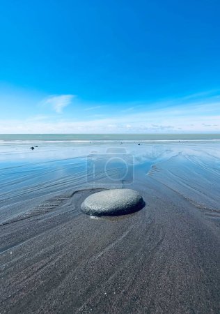 Foto de Un plano vertical de una playa con piedras bajo un cielo azul, arenas volcánicas negras, Waitara Beach, Taranaki, Nueva Zelanda - Imagen libre de derechos