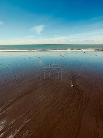 un plano vertical de una playa con piedras bajo un cielo azul, arenas volcánicas negras, Waitara Beach, Taranaki, Nueva Zelanda