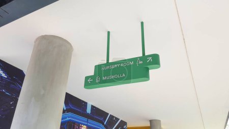 Photo for Jakarta Indonesia August 22 2023: A ceiling hung green  directional signage to nursery room and musholla praying room - Royalty Free Image