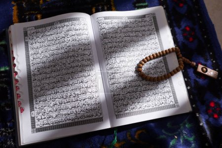 Großaufnahme von hölzernen Gebetsperlen, die auf dem offenen Koran liegen