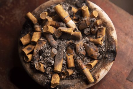 Photo for Dirty ashtray full of cigarette butts on a wooden table - Royalty Free Image