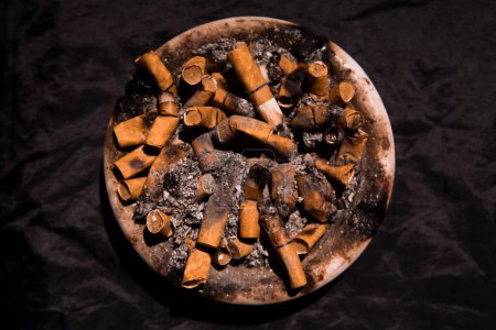 Photo for Dirty ashtray full of cigarette butts with black background - Royalty Free Image