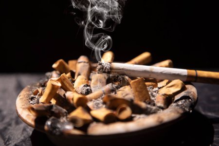 Photo for Cigarettes burning with smoke in ashtray full of cigarette butts - Royalty Free Image