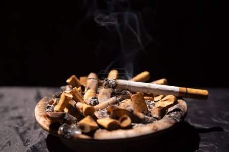 Photo for Cigarettes burning in ashtray full of cigarette butts - Royalty Free Image