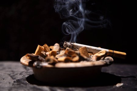 Photo for Cigarettes burning with smoke in the ashtray with black background - Royalty Free Image