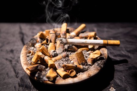 Photo for High angle view of cigarettes burning with smoke on the ashtray - Royalty Free Image