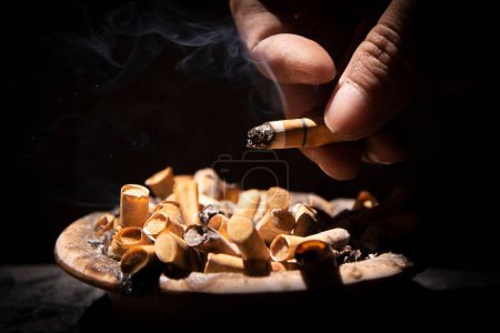 Photo for Flicking cigarette ash from cigarette into ashtray with black background - Royalty Free Image