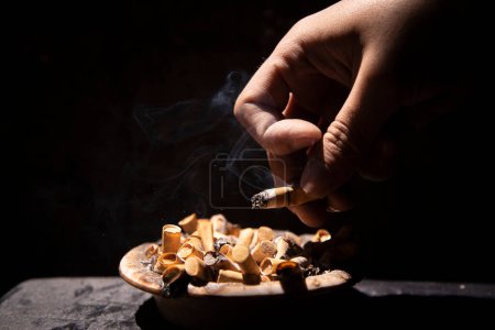 Photo for Flicking cigarette ash from cigarette into dirty ashtray - Royalty Free Image