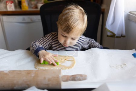 Photo for Family cooking - a little boy pushes in a cutting cookie mold onto the raw dough. Mid shot - Royalty Free Image