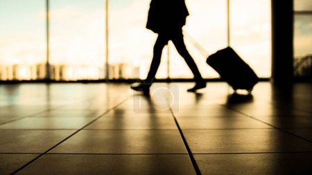 Téléchargez les photos : Voyageur à l'aéroport marchant vers les départs devant la fenêtre, couleurs chaudes - en image libre de droit