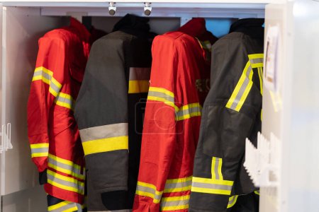 Photo for Red firefighter jackets and helmets on a wall rack, ready for use. - Royalty Free Image