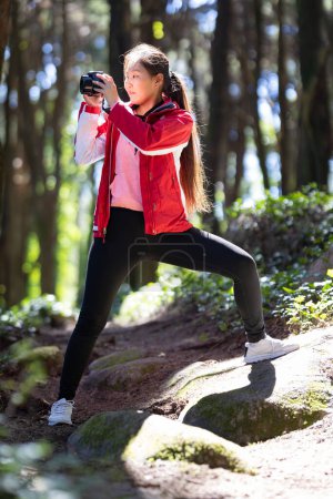A woman wearing a red jacket is gracefully performing a yoga pose outdoors with friends. Her focused stance and perfect form demonstrate strength and flexibility.