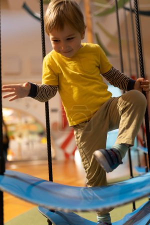 Foto de Un niño está jugando en un columpio. Lleva una camisa amarilla y pantalones caqui. - Imagen libre de derechos
