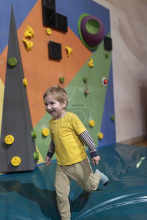 Foto de Un niño está corriendo sobre una superficie azul con una camisa amarilla. Él sonríe y se divierte. - Imagen libre de derechos
