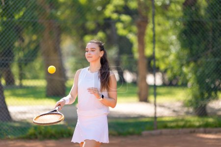 A woman is playing tennis with a tennis ball. She is wearing a white dress and a white wristband