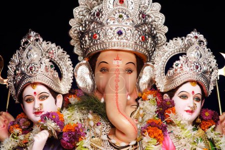 Richly decorated idol of lord ganesh elephant headed god sitting with his two consorts Riddhi and Siddhi for Ganpati festival at Mandai , Pune , Maharashtra , India