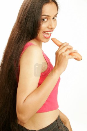 Südasiatische indische Teenager-Mädchen mit lockeren schwarzen dicken und langen Haaren beißen rohes Karottengemüse gut für die Gesundheit 