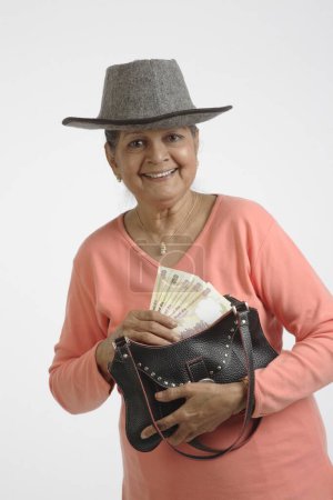 Alte Dame mit fünf Scheinen zu je 500 Rupien in der einen Hand und einer Handtasche in der anderen 