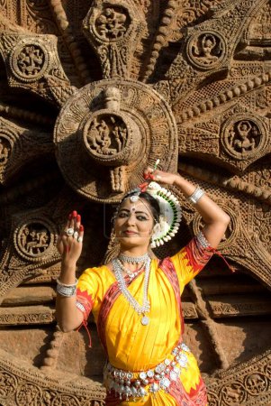 Téléchargez les photos : La pose de la danseuse Odissi reproduit des mythes indiens tels que le Ramayana devant l'emblématique Sun Chariot dans le complexe du temple solaire du patrimoine mondial à Konarak, Orissa, Inde - en image libre de droit