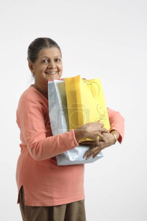 Old lady holding colorful shopping bags near her chest and smiling 