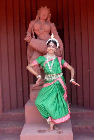 Photo for Woman performing classical traditional Odissi dance in front of statue on stage - Royalty Free Image